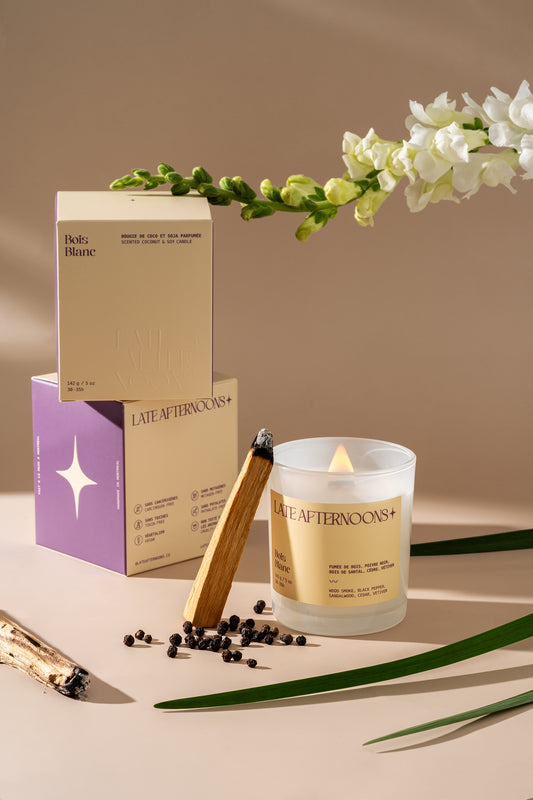Bougie Bois Blanc allumée avec ses boîtes, des fleurs blanches, du palo santo et du poivre noir