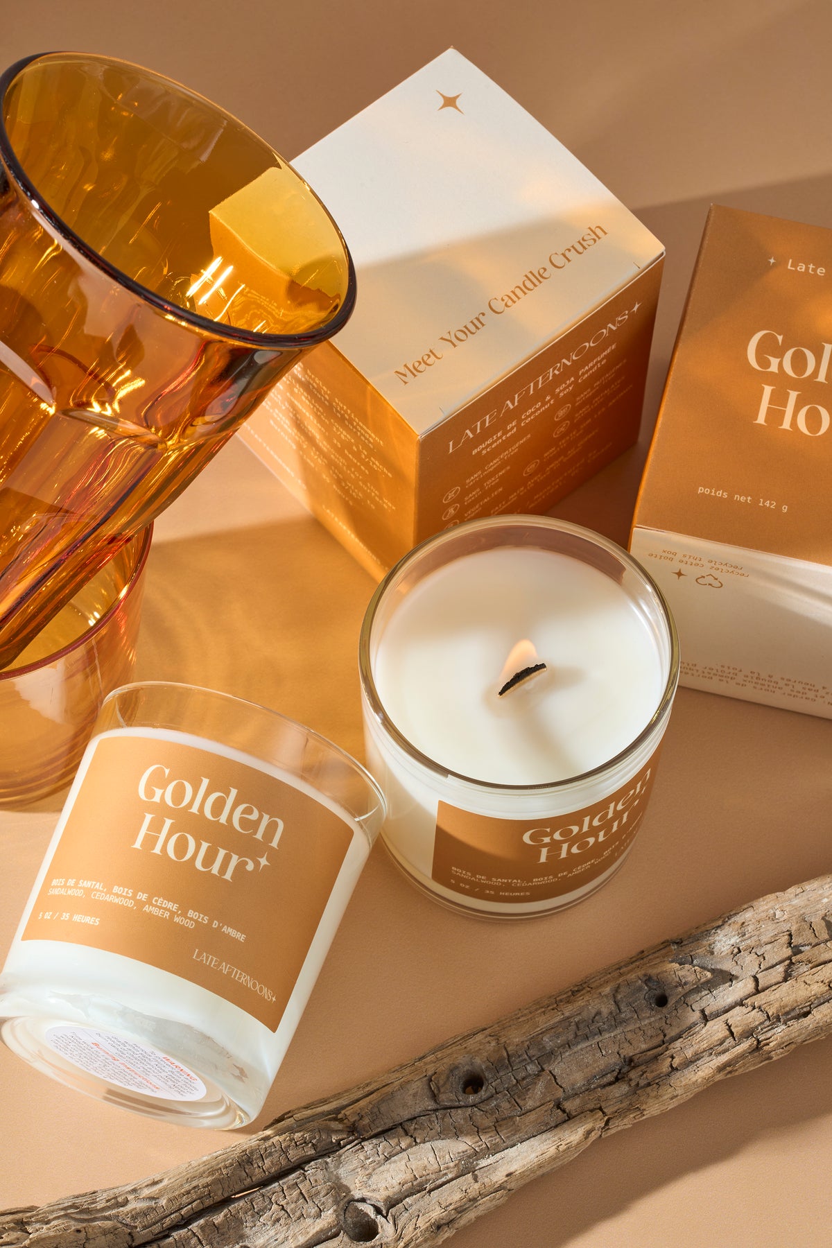 Bougie Golden Hour allumée avec un verre ambré, ses boîtes et du bois flotté