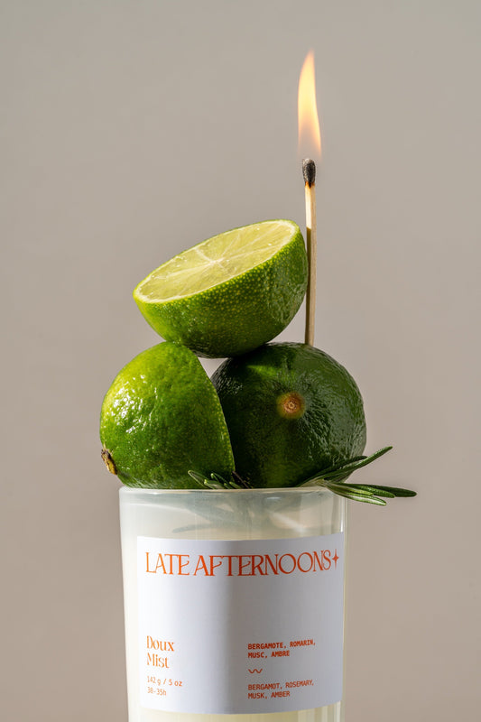 A Late Afternoons candle burning, styled with limes and rosemary