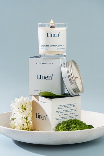 Candle labeled 'Linen' with packaging and decorative elements on a light blue background