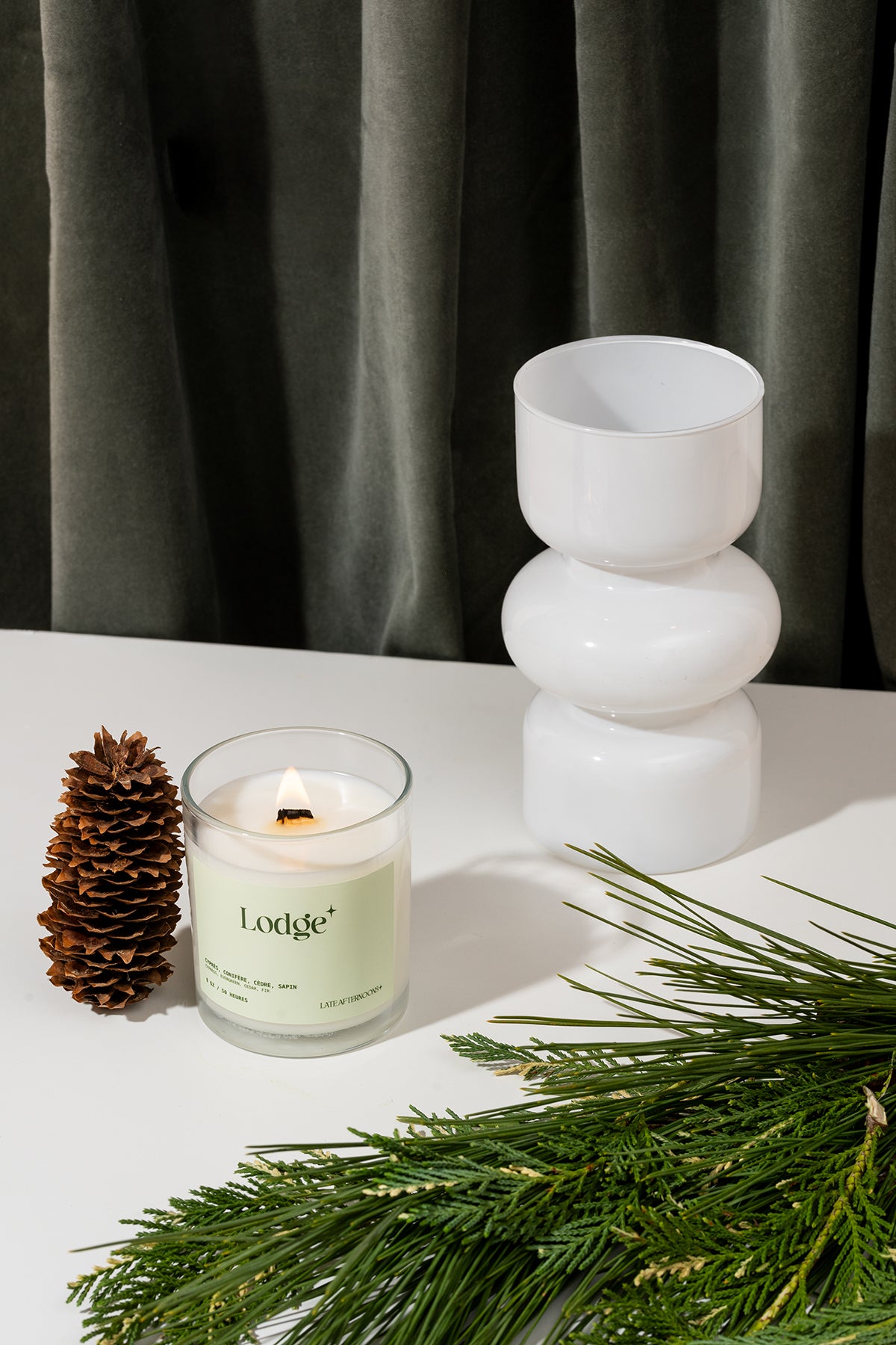Lit Lodge candle styled with pine branches and a pinecone by Late Afternoons