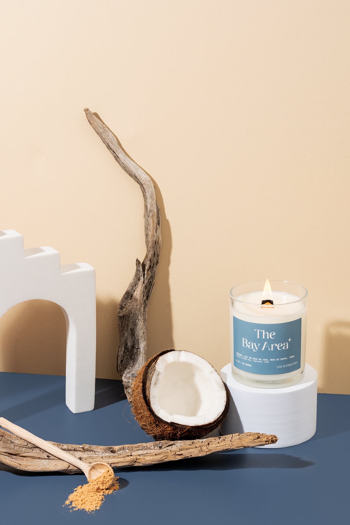 The Bay Area candle lit with driftwood, a halved coconut and a white arch