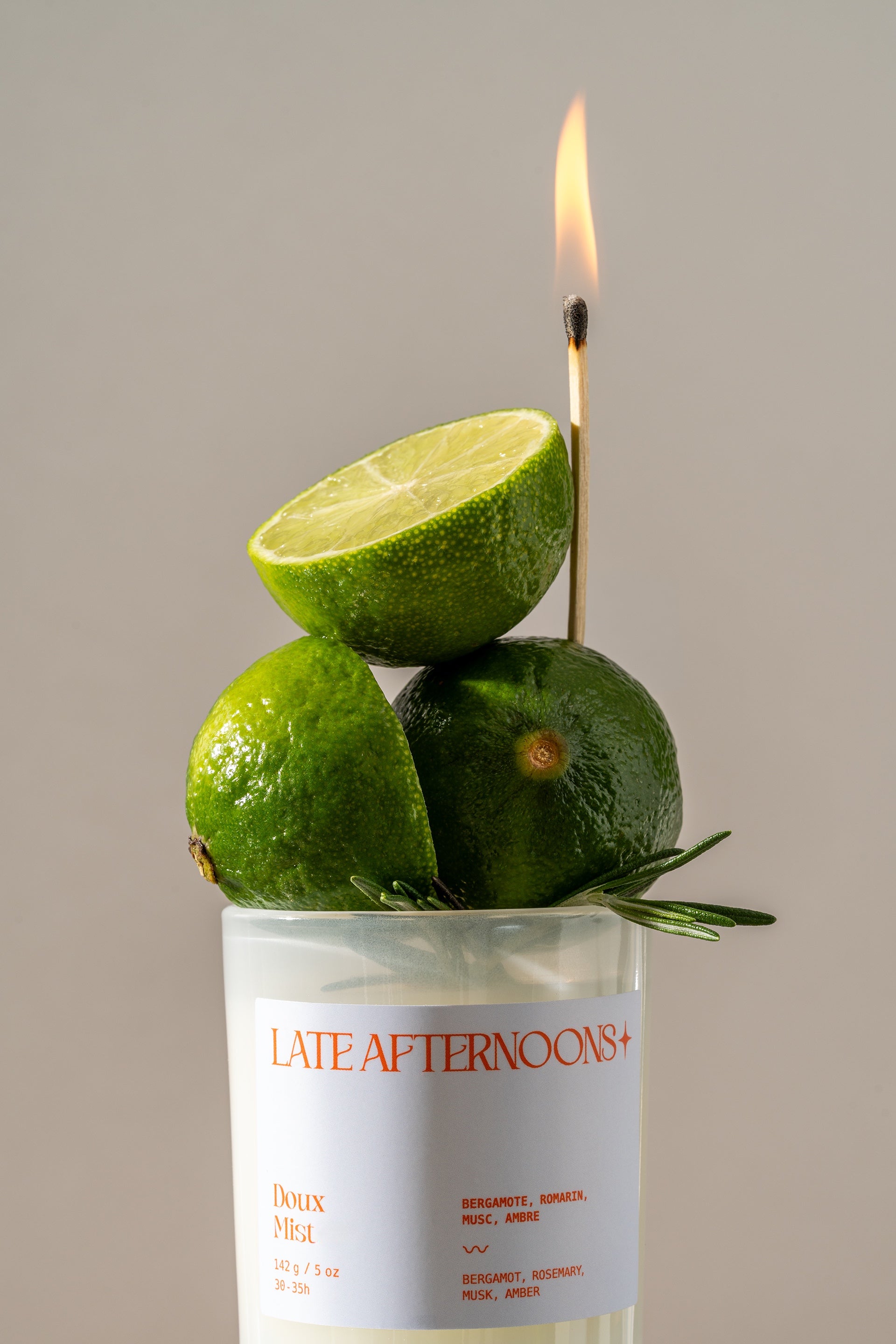 Doux Mist 5 oz candle topped with fresh limes and rosemary, a lit match above, coconut soy by Late Afternoons
