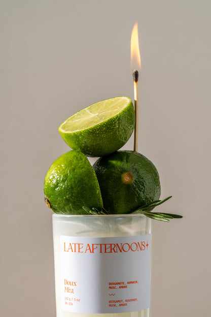 Doux Mist 5 oz candle topped with fresh limes and rosemary, a lit match above, coconut soy by Late Afternoons