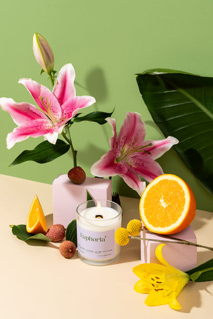 Bougie Euphoria allumée avec lys roses, litchis et orange sur fond vert