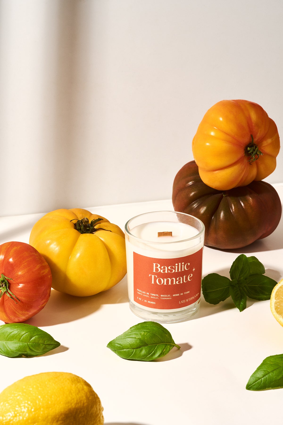 Bougie Basilic Tomate allumée avec des tomates ancestrales empilées, du basilic et un citron